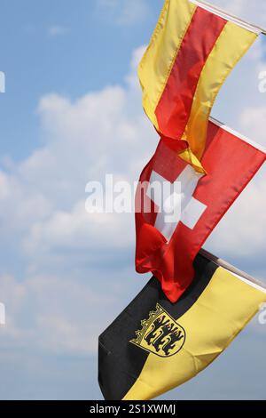 Drei Fahnen auf den Fahnenmasten - winken im Wind. Flaggen von Baden, Schweiz, Flagge Baden-Württemberg mit einem Emblem. Schweizer Flagge in der Mitte. Isola Stockfoto