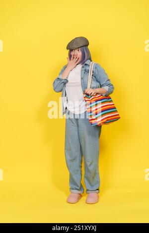 Frau in blauer Jacke und Jeans hält eine bunte Tasche. Sie trägt einen Hut und hat einen überraschenden Gesichtsausdruck Stockfoto