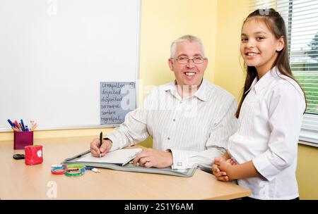 Junior School: Schüler der Klasse A. Eine Juniorschullehrerin, die die Arbeit eines jungen Mädchens im Klassenzimmer bewertet. Stockfoto