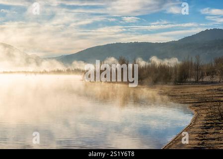 Ein nebeliger Morgen an einem See mit Wolken und Bergen im Hintergrund. Stockfoto