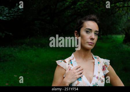 Wunderschöne junge Brünette, die draußen in einem ländlichen Waldgebiet ein Sommerkleid trägt Stockfoto
