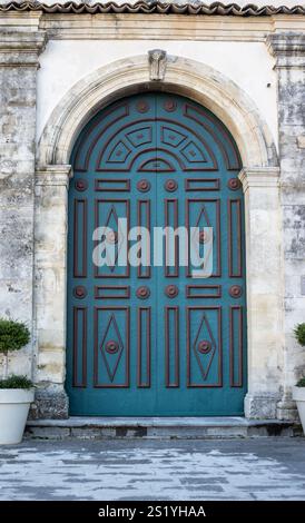 Grünes verziertes geschlossenes Tor mit Ornamenten und einem Bogen. Blumen in Pfosten auf beiden Seiten. Straße in der historischen Barockstadt Ragusa, Sizilien, Italien. Stockfoto