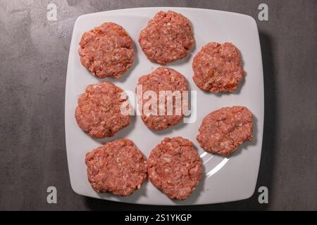 Rohe, hausgemachte Burger Patties aus Hackfleisch, ordentlich auf einem weißen Teller angeordnet, fertig zum Kochen. Stockfoto