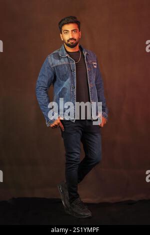 Ein indisches männliches Model posiert in Jeansjacke und Jeans vor grauem Hintergrund in voller Länge Stockfoto