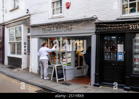 Eine junge Frau reinigt das Fenster von Paxton und Whitfield Cheesemongers, Palace Street, Canterbury, Kent, Großbritannien. Stockfoto