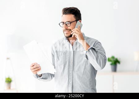 Home Office-Konzept. Selbstbewusster Millennial-Unternehmer, der am Handy spricht und Finanzberichte diskutiert Stockfoto