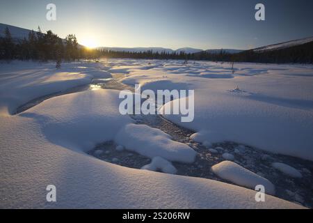 Wunderschöne arktische Winterlandschaft mit verschneiten Wäldern im Hintergrund, blauem Himmel und Sonnenuntergang am Horizont. Kaltes Klima Stockfoto