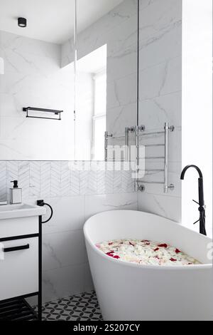 Ein elegantes, modernes Badezimmer mit einer beruhigenden Badewanne mit wunderschönen Blütenblättern Stockfoto