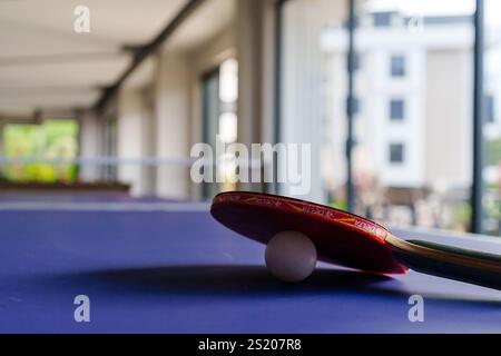 Ein Tischtennisschläger und -Ball auf einem blauen Tisch, der die Essenz dieses klassischen Sports einfängt. Stockfoto