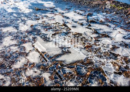 Gefrorenes Wasser bildet rutschiges Eis am Straßenrand Stockfoto