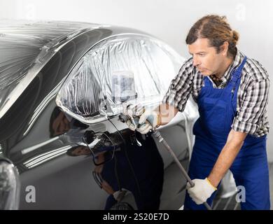 Mann mittleren Alters mit Spritzpistole, um Auto in der Werkstatt zu lackieren Stockfoto