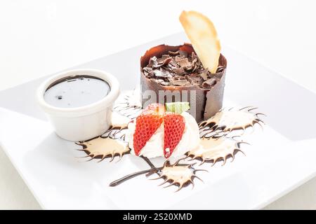 Ein Dessertteller mit Schokoladenkuchen und Erdbeeren. Der Teller ist weiß und das Dessert wird mit Schokoladensauce belegt Stockfoto