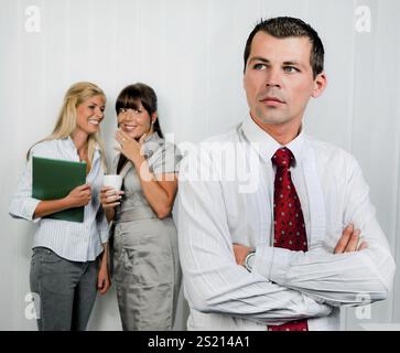 Mobbing am Arbeitsplatz in einem Büro. Frauen machen sich über Männer lustig Österreich Stockfoto