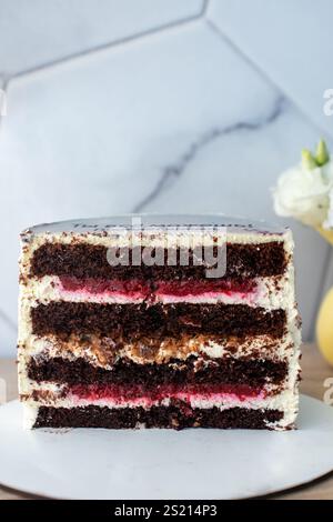 Nahaufnahme von Schokoladenschichtkuchen mit Sahne- und Beerenfüllung auf weißer Platte vor Marmorhintergrund. Stockfoto