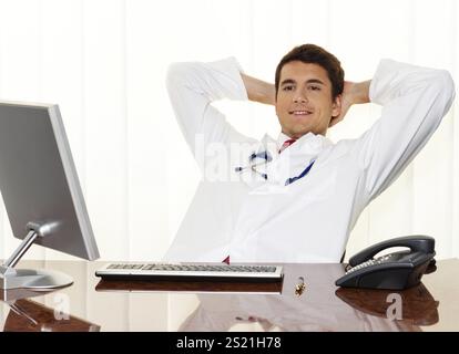 Ein erfolgreicher junger Arzt sitzt an seinem Schreibtisch und lächelt. Österreich Stockfoto