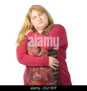 Eine Frau mit langen blonden Haaren umarmt sich mit geschlossenen Augen und drückt Selbstliebe und Trost aus. Sie trägt einen roten und gemusterten Pullover ag Stockfoto