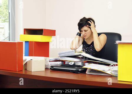 Verzweifelte, gestresste Frau, die an ihrem Schreibtisch sitzt und den Kopf hält, mit Arbeit überlastet Stockfoto