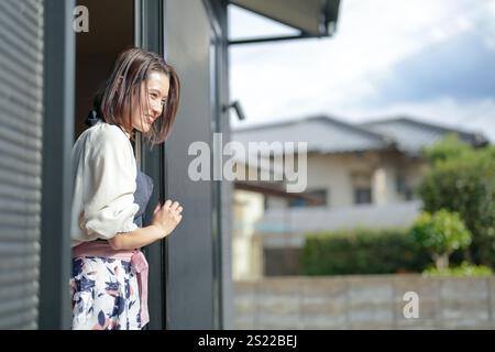 Eine Japanerin in den 30ern streckt ihren Körper aus dem Fenster ihres Hauses und schaut nach draußen. Stockfoto