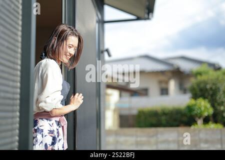 Eine Japanerin in den 30ern streckt ihren Körper aus dem Fenster ihres Hauses und schaut nach draußen. Stockfoto
