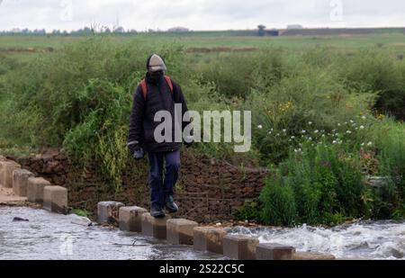 Johannesburg, Südafrika - ein unbekannter Mann benutzt das Betonbollwerk, um eine überflutete Niedrigwasserbrücke über den Klip südlich der Stadt zu überqueren Stockfoto