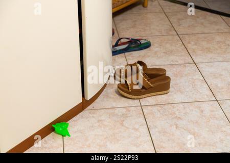 Braune Frauen-Maultiere und Flipflops vor einem Schrank auf einem Fliesenboden Stockfoto