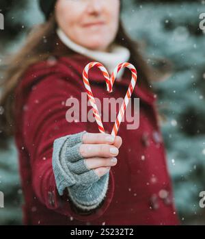 Eine Frau im roten Mantel, die im Schnee Zuckerstöcke in Herzform hält. Stockfoto
