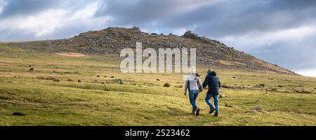 Ein Panoramablick von zwei Personen, die auf den imposanten Granitgrat Roughtor Rough Tor auf dem wilden windgepeitschten Bodmin Moor in Cornwall in t gehen Stockfoto