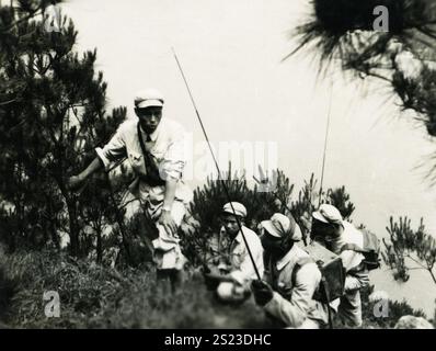 Soldaten, die bei Sonnenaufgang in einem bewaldeten Gebiet einen Hügel besteigen, gekleidet in leichte Uniformen und ausgerüstet für eine Übung: 1950er Jahre PLA Field Radio Operation: Ein Blick in die chinesische Militärkommunikationsgeschichte. Stockfoto