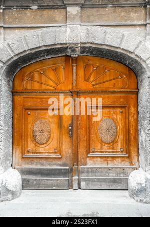 Alte Holztür mit Rundbogen und Dekorationen. Rustikaler breiter Eingang in braunem Grau. Stockfoto