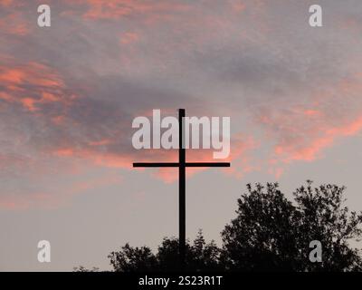 Ein einfaches hölzernes Kreuz aus dünnen Dielen mit einem eisernen Ring oben, das auf einem Dais vor dem Hintergrund von Ästen und einem wunderschönen Himmel steht Stockfoto