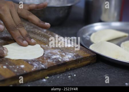 Nahaufnahme der Hände, die Teig auf einer Holzoberfläche Formen, mit vorbereiteten Knödeln auf einer Metallplatte im Hintergrund – Zubereitung und Kochen von Lebensmitteln. Stockfoto