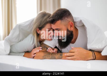 Das junge, glückliche Liebespaar liegt morgens im Bett. Sie sind sehr umgangssprachlich. Stockfoto