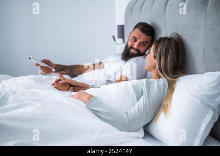 Das junge Paar liegt abends im Bett. Sie schauen fern und machen sich bereit für den Schlaf. Stockfoto