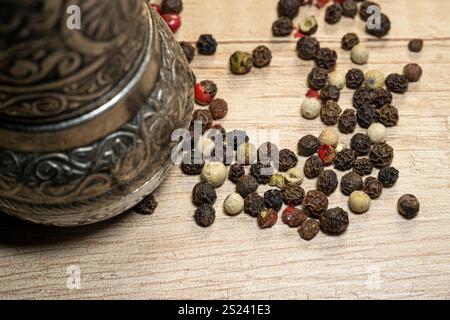 Gewürzmühle und Pfefferkörner aus nächster Nähe. Pfeffermühle mit Pfeffermischung auf einem Holztisch. Stockfoto