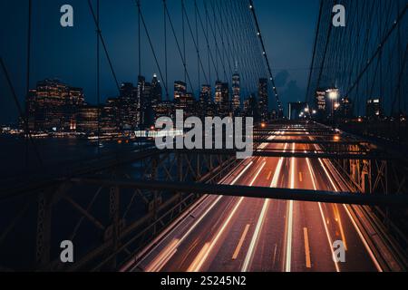 Ein Langzeitfoto von Autolichtern, die über die Brooklyn Bridge strömen, mit der beleuchteten Skyline von Manhattan im Hintergrund. Stockfoto