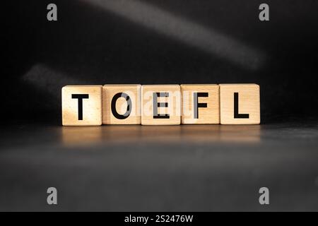TOEFL auf Holzblöcken geschrieben (Test of English as a Foreign Language) Conceptual Slogan. Schöner schwarzer Hintergrund, natürlich beleuchtet Stockfoto