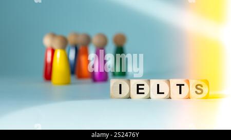 IELTS auf Holzblöcken geschrieben (International English Language Testing System) Conceptual Slogan. Hellblauer Hintergrund, mehrfarbige menschliche Figuren, Stockfoto