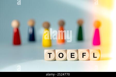 TOEFL auf Holzblöcken geschrieben (Test of English as a Foreign Language) Conceptual Slogan. Hellblauer Hintergrund, mehrfarbige menschliche Figuren. Stockfoto