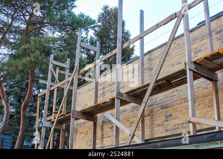 Die Arbeiter bereiten sich darauf vor, eine Ziegelmauer mit Gerüsten in einer von Bäumen umgebenen Umgebung zu renovieren. Stockfoto
