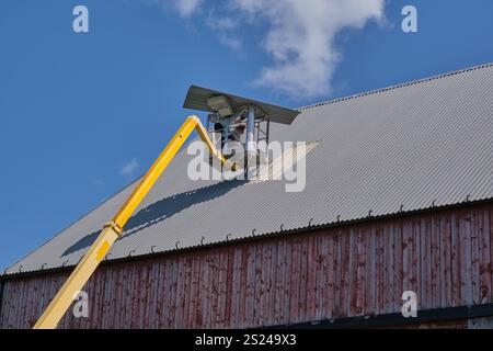 Reparatur des Dachs eines landwirtschaftlichen Gebäudes mit einer Hebebühne auf einem Bauernhof in Skaraborg Schweden an einem sonnigen Sommertag im August Stockfoto