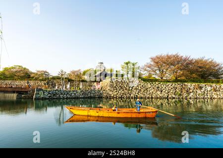 Ein Punt mit zwei Touristen, die an einem sonnigen Frühlingstag während der goldenen Stunde im Frühling am Tor der Burg Himeji vorbeigerudert werden. Stockfoto