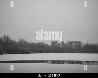 Prag, Tschechische republik - 27. Dezember 2024: Schneebedeckte Landschaft mit einem gefrorenen Seeteich, der Wohngebäude in prag 9, tschechien, während A reflektiert Stockfoto
