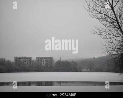 Prag, Tschechische republik - 27. Dezember 2024: Schneebedeckte Landschaft mit gefrorenem See reflektierende Gebäude an einem bewölkten Wintertag in prag 9, tschechien Natur p Stockfoto