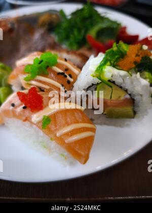 Frisch zubereitetes Sushi mit Lachsnigiri und Maki-Rollen, einladend auf einem weißen Teller mit lebhaften Farben und Texturen Stockfoto