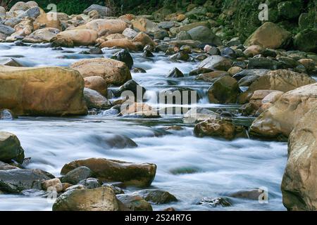 Ein schnell fließender Fluss stürzt über glatte und raue Felsen und schafft eine dynamische Wasserszene. Das Wasser scheint aufgrund einer langen Exposition verschwommen zu sein. Befindet sich in Stockfoto