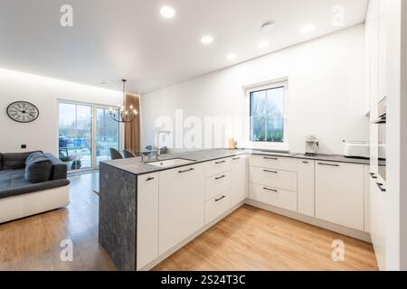 Moderne Küche in weiß und Grau mit stilvollem minimalistischem Design. Heim Wohnzimmer Inneneinrichtung mit Glastisch und großen Fenstern. Sofa, Couch in Ba Stockfoto