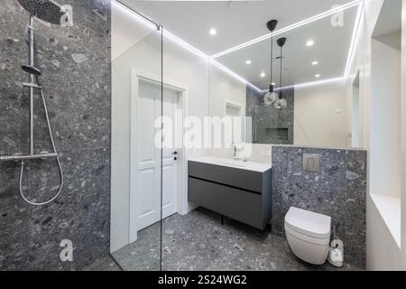 Modernes Bad mit grauem Fliesenboden, minimalistischem grauen Kosmetikbereich, weißen Wänden und eingelassener Beleuchtung für einen sauberen, stilvollen Look Stockfoto