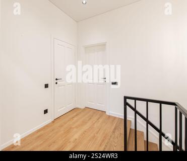 Ein heller, minimalistischer Innenkorridor mit Holzfußboden, weißen Wänden und Türen mit modernen Griffen. Ideal für Immobilien, Innenarchitektur, o Stockfoto