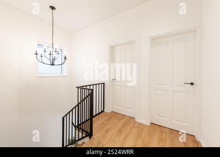 Ein minimalistisches, modernes Haus, Hausflur mit warmem Holzboden, eleganter schwarzer Geländertreppe, weißen Paneeltüren, beleuchtet von einem Contempo Stockfoto