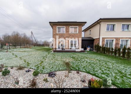 Ein Backsteinhaus mit Terrasse und Einfahrt. Das Haus ist von einem schneebedeckten Hof umgeben. Zwei benachbarte zweistöckige Häuser mit Ziegelfassaden und Putz Stockfoto